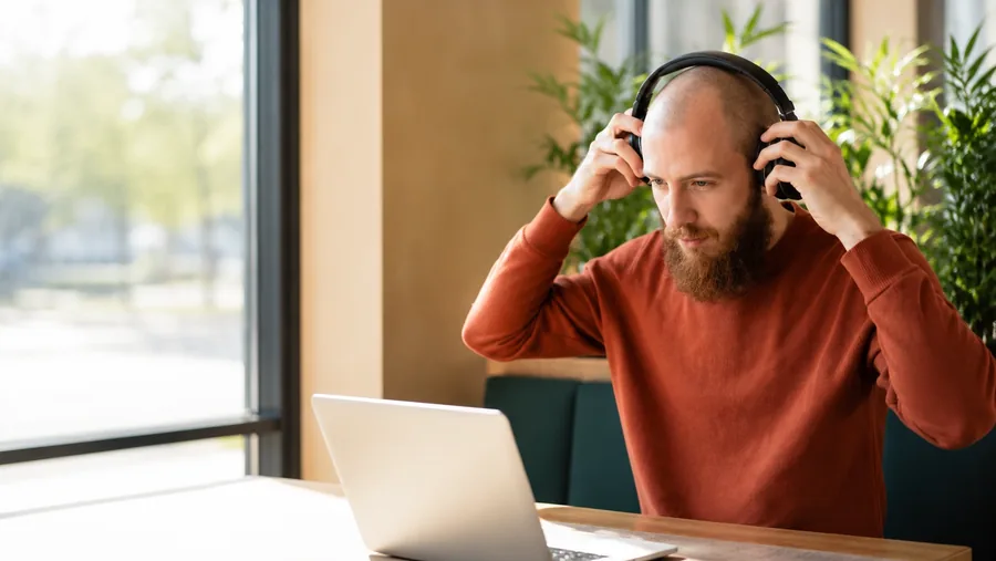 A practitioner putting on headphones before a call, in a plant-filled office by a window