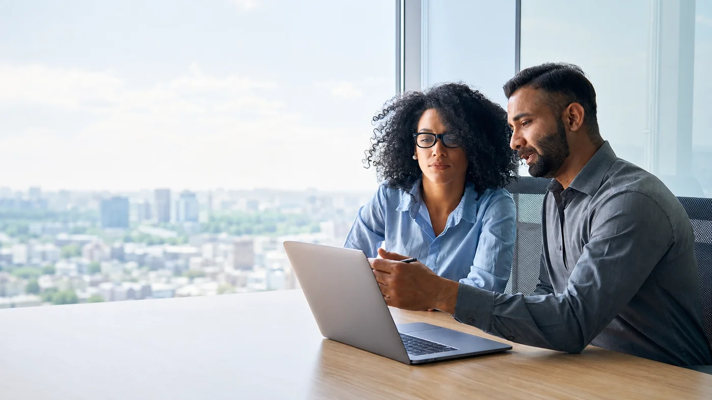 Two practitioners reviewing strategy together on a laptop in a high-rise office overlooking the city